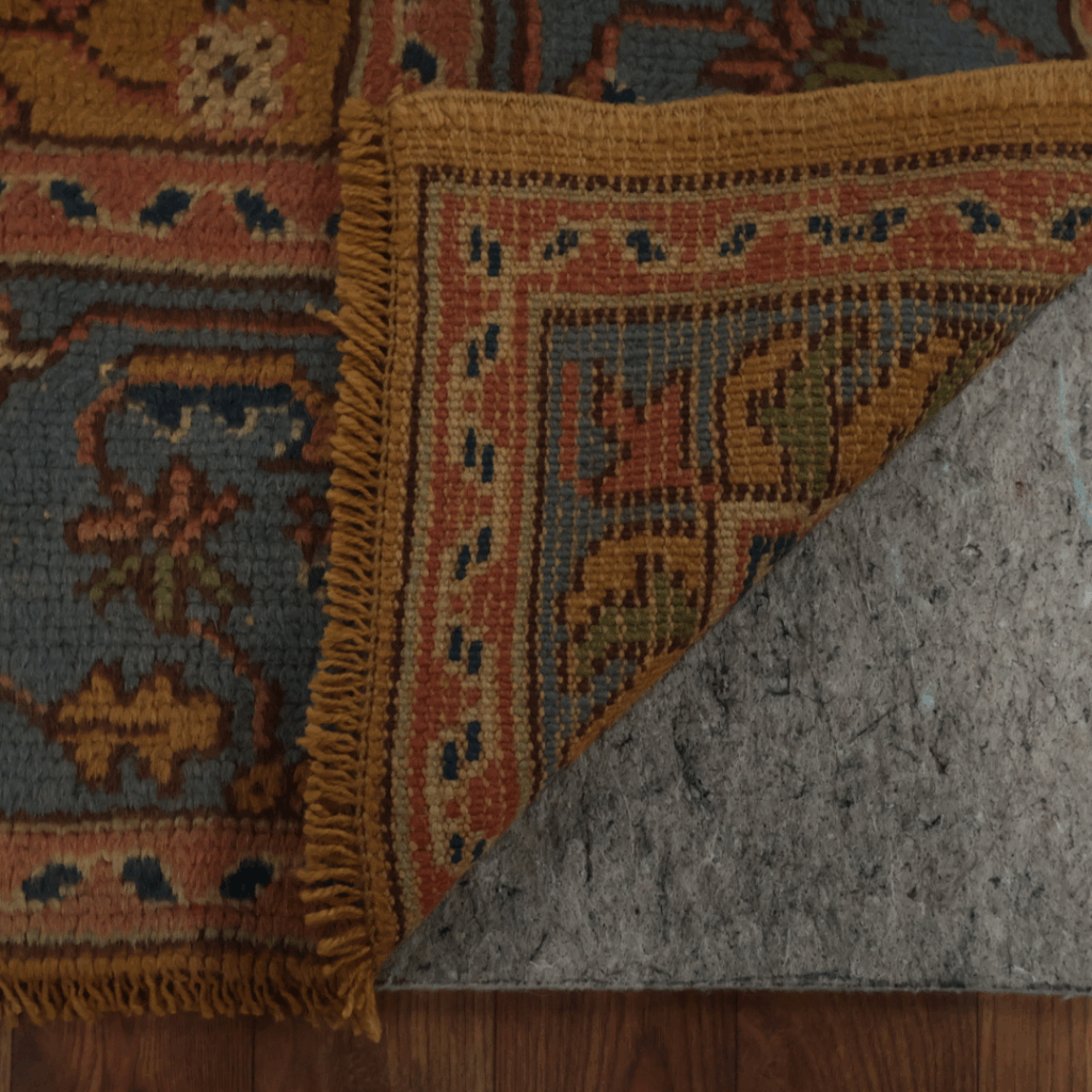 10_20 Another close-up of the same traditional rug, showing its detailed woven border in warm orange, gold, and blue tones against a gray field.