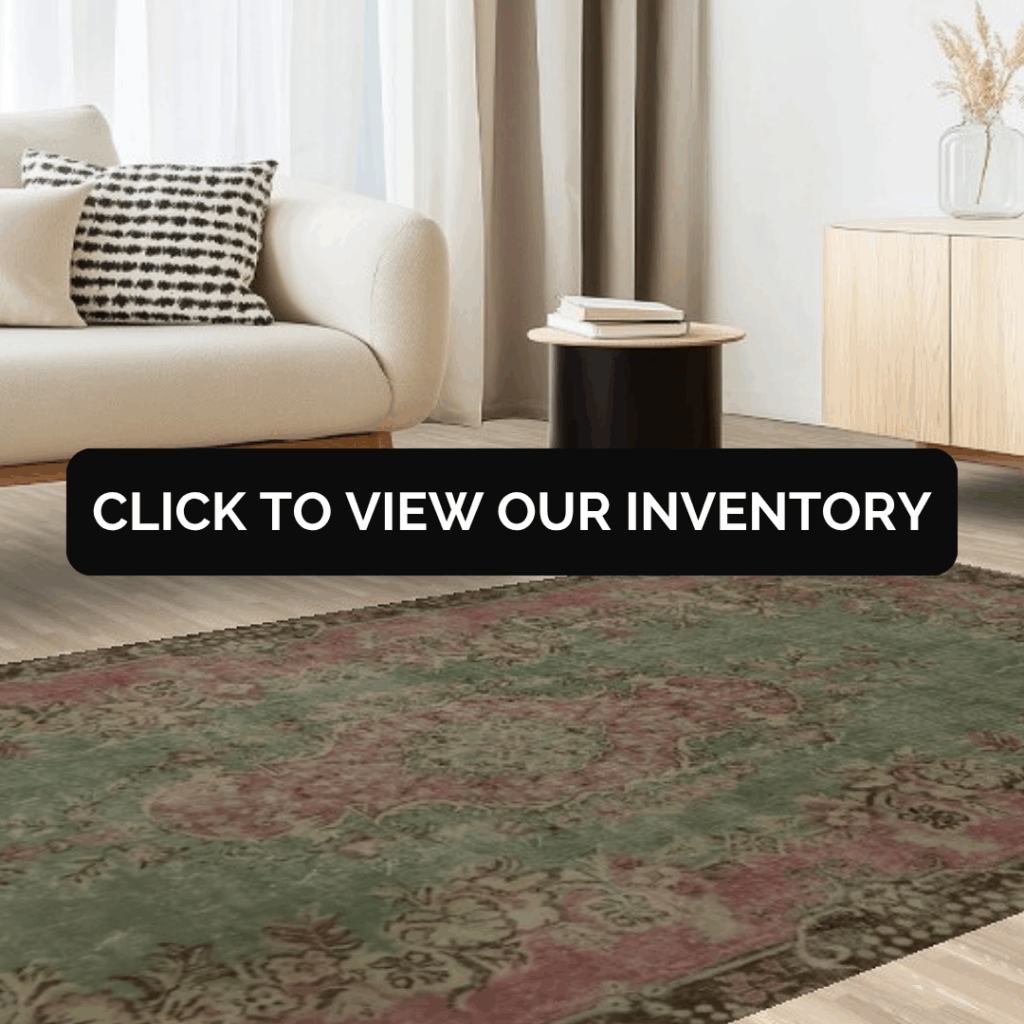 A modern living space featuring a cream-colored sofa with a black-and-white patterned pillow, beside a sleek black side table and light wood cabinet. A vintage-style green and red rug covers the floor, overlaid with the text, “Click to view our inventory.”