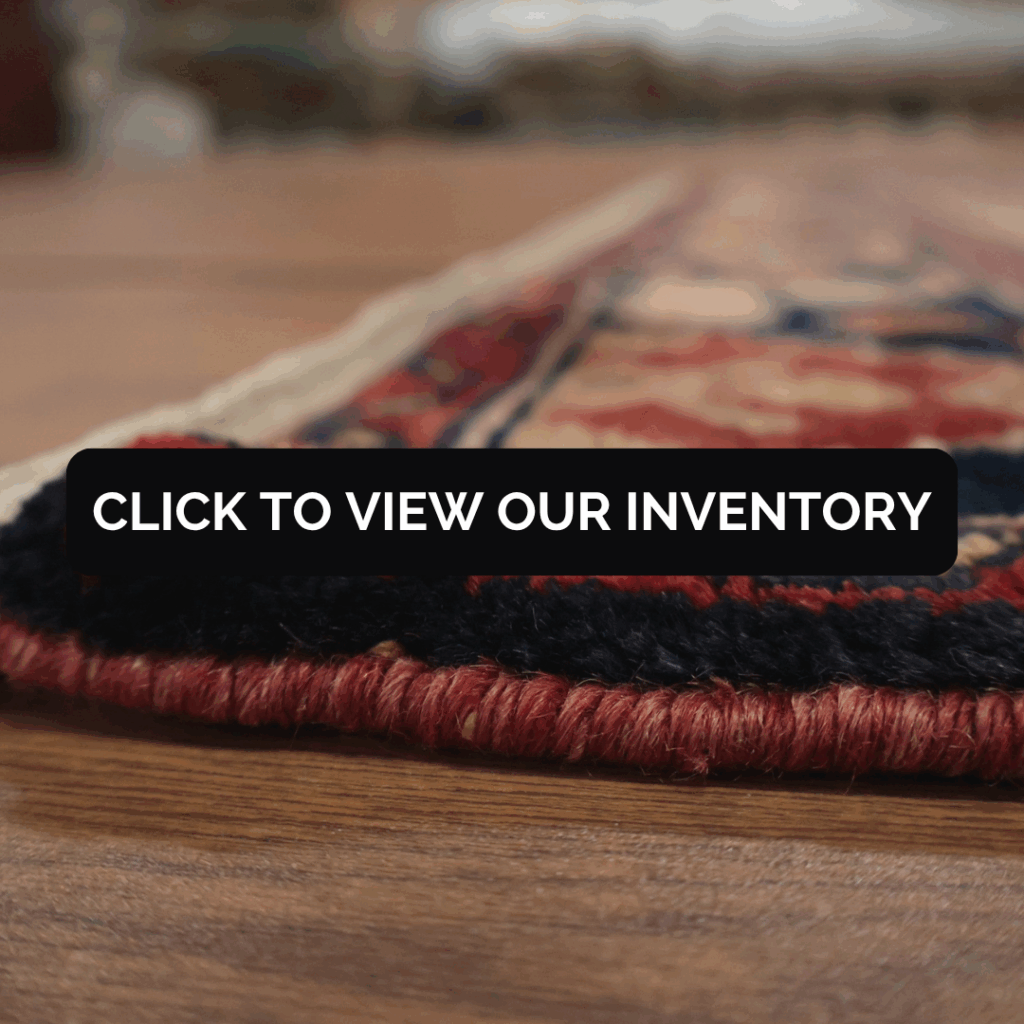 A close-up, side view of a handwoven rug with red, navy, and beige details lying on a wooden floor. A black banner across the center reads, “Click to view our inventory.”