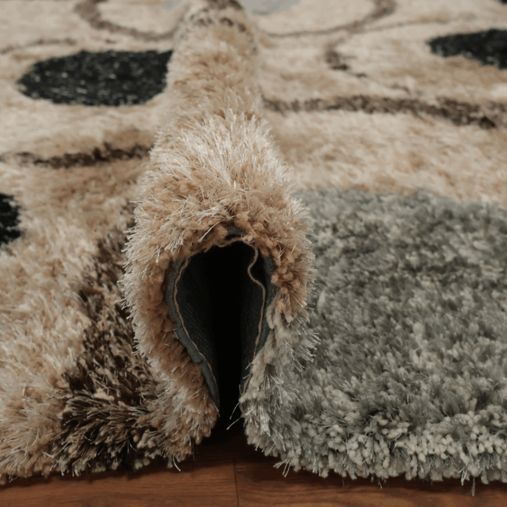 A thick shag rug in neutral beige, gray, and black tones, shown folded to highlight its fluffy texture.
